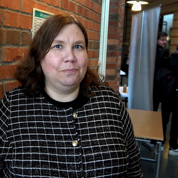 Sophie Blomback, a political scientist, stands in front of a brown brick wall in a building at Mituniversität in Sundsvall.