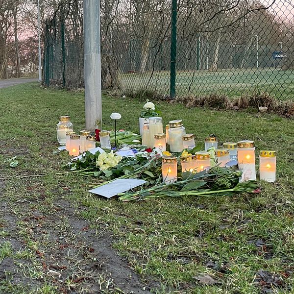 Minnesplats med ljus och blommor vid en parkstig.