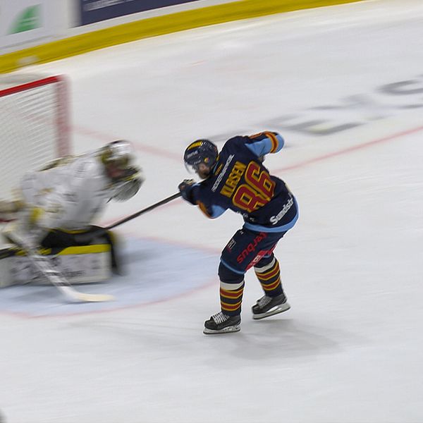 Ishockeyspelare skjuter mot mål, målvakten försöker rädda pucken med benskydden.
