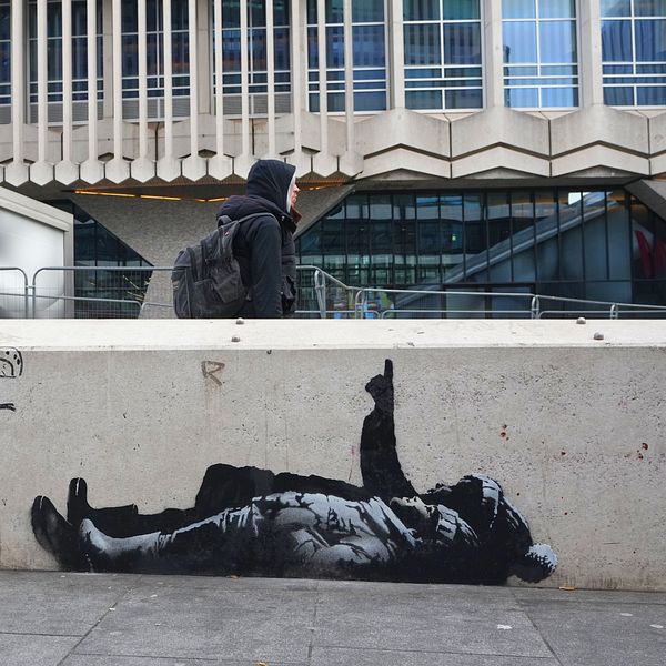 En hund utanför tunnelbanestation i London vid nytt gatukonstverk av Banksy på väggen.