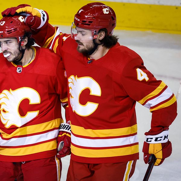 Två hockeyspelare i Calgary Flames firar ihop på isen i röda matchtröjor.