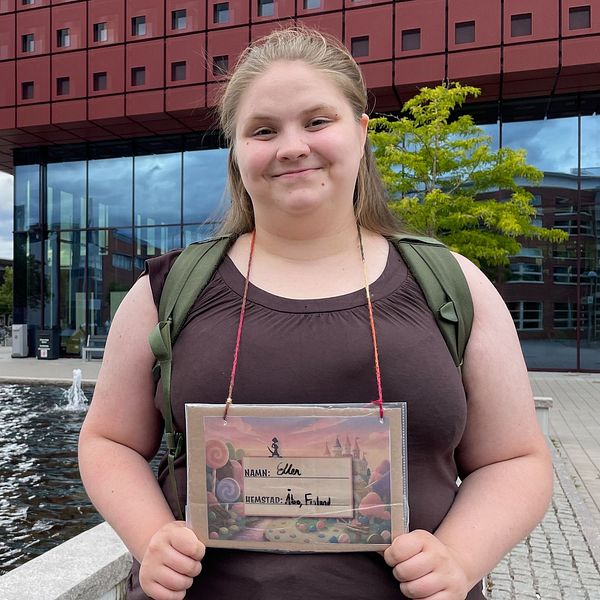 Ellen Karlsson yliopistorakennuksen edessä kyltti kaulassa, jossa lukee hänen nimensä ja kotipaikkakuntansa.