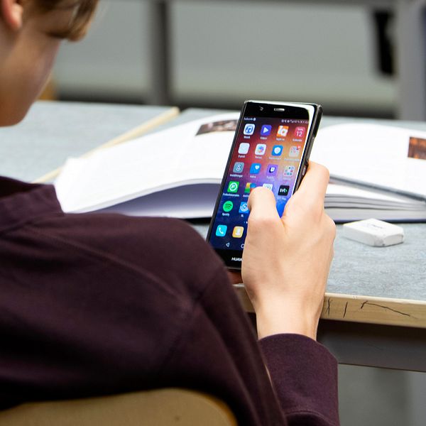 Ung kille sitter med mobiltelefon i en skolsal.