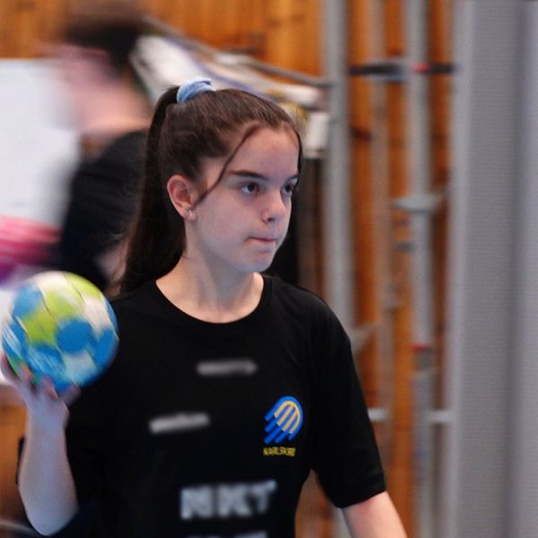 Handbollsspelare med boll i handen under en inomhusträning. Trävägg och whiteboard i bakgrunden.