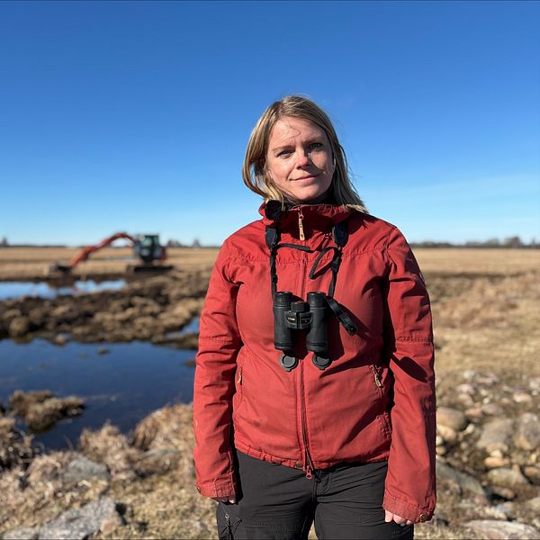 Fia Sundin vid våtmark med grävmaskin i bakgrunden under restaureringsarbete.