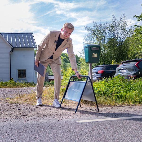 Fastighetsmäklaren David Töyrylä ställer ut en skylt med texten ”visning”. I bakgrund syns en vit villa.