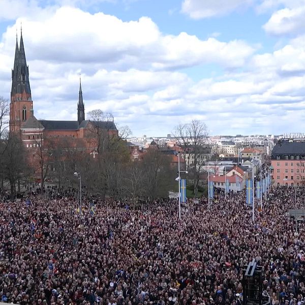 Man med grön tröja och brunt hår och kyrka med massor av folk