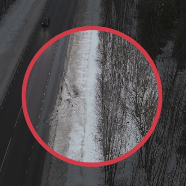 En väg med snö på kanterna, där ett cirkelformat område markerar en del av den snötäckta vägkanten med några träd i bakgrunden.