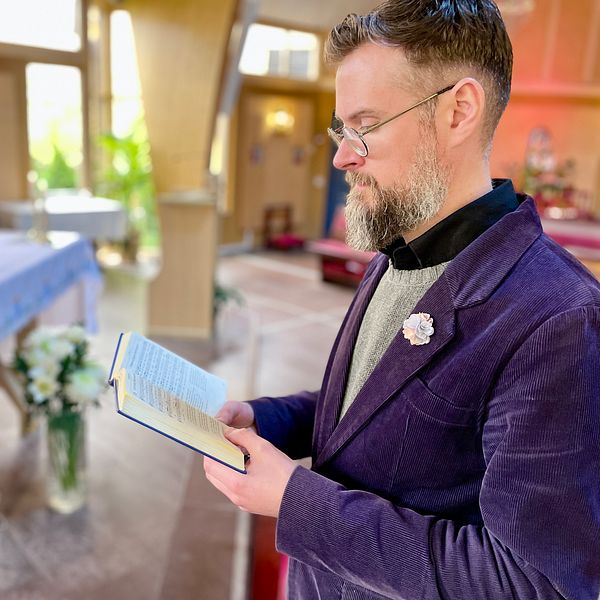Man i kostym håller i en bok framför ett altare i en kyrka.