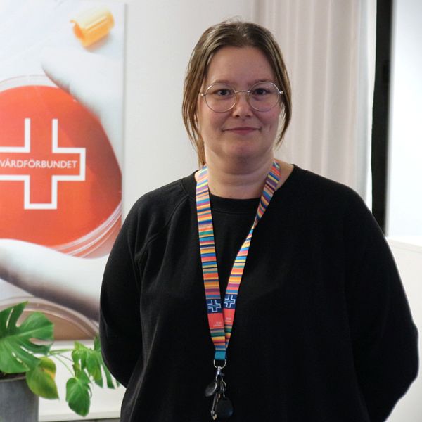 Bilden är en delad bild. Till vänster står en person i SVT-jacka med en mikrofon utomhus framför en byggnad. Till höger står en annan person inomhus, framför en affisch med Vårdförbundets logotyp, och bär en färgglad halsbandshållare.