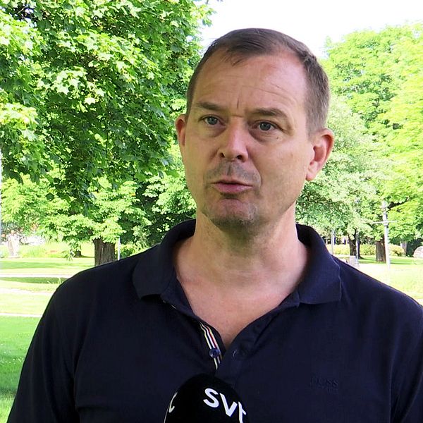 Magnus Lindström står i en grön park med träd och gräsmatta runt omkring. I bakgrunden syns en parkbänk och en lekplats. Han pratar i en mikrofon med en logotyp från SVT.