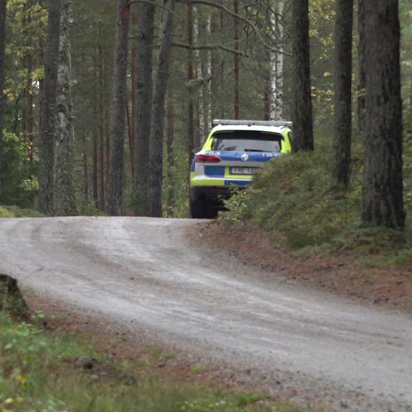 Grusväg, en polisbil står parkerad i en kurva till höger i bild.