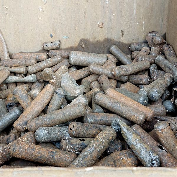 Bild med två sektioner: till vänster syns en hög med skräp, främst trasiga kläder och textilier, hängande från en vägg, medan höger sektion visar en behållare fylld med rostiga metallcylindrar, troligtvis gamla patroner eller liknande.