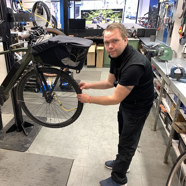 En cykel är upphissad på en verkstad, där Mikael Lipponen står och känner på framhjulet.