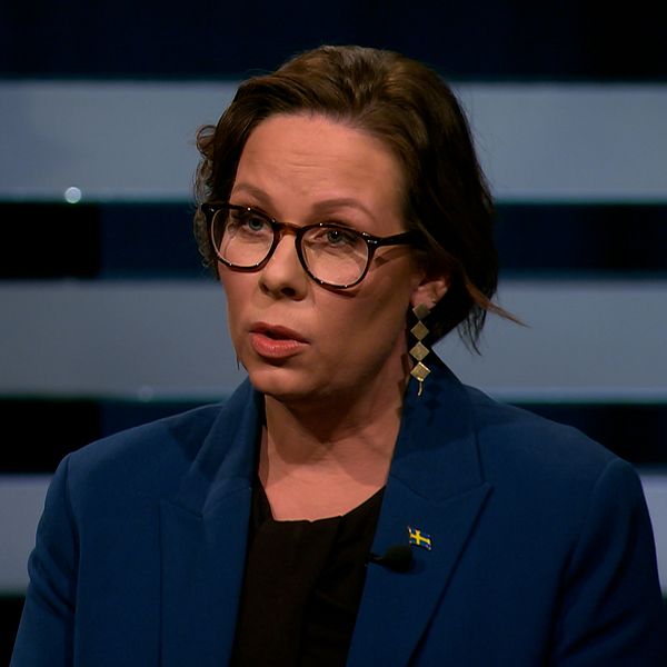 Två personer står mitt emot varandra i en tv-studio under en intervju eller debatt.
