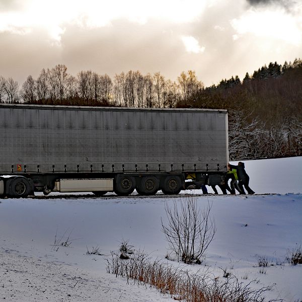 Folk puttar på en lastbil som kört fast i snön.