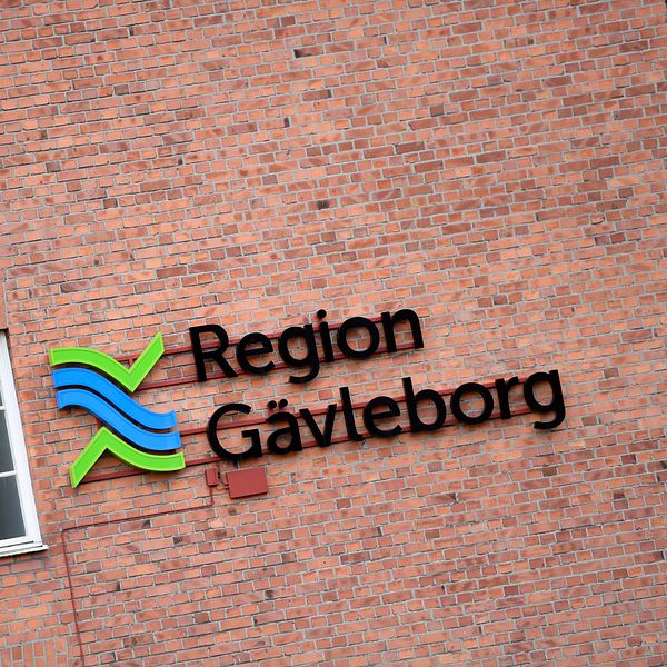 Region Gävleborgs logga på en röd tegelvägg vid ett fönster.