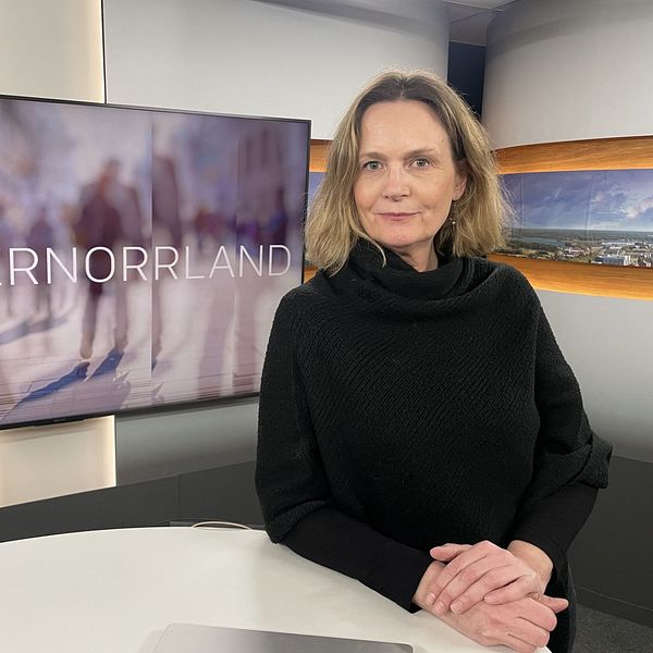 En kvinna med svart tröja och ljust hår ståendes vid ett bord.