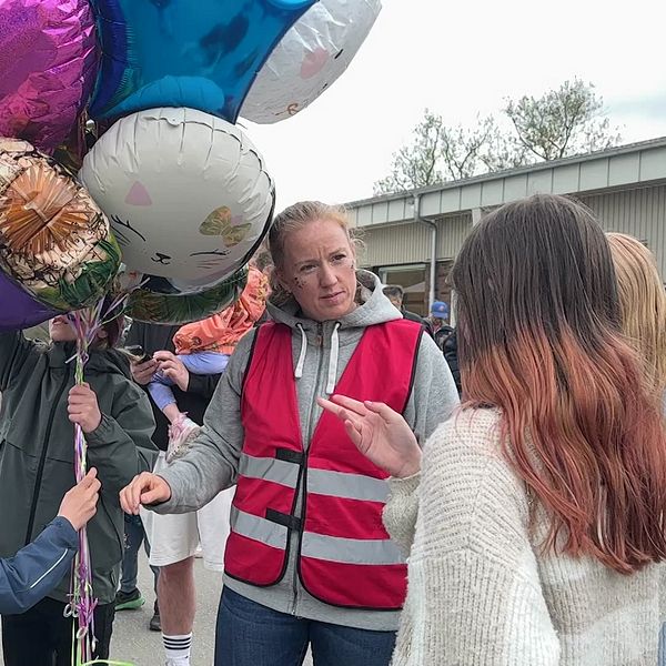 Person i röd väst delar ut heliumballonger till barn och vuxna vid en utomhusaktivitet.