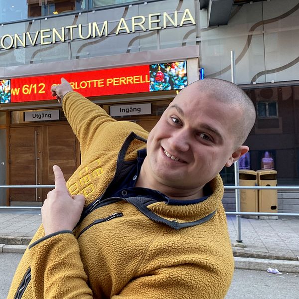 En man som ler och pekar på den stora arenabyggnaden Conventum i Örebro bakom sig.
