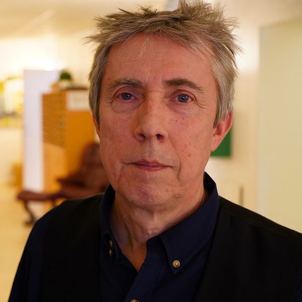 Gunnar Bergström, professor i arbetshälsovetenskap, står i mörkblå skjorta på campus i Högskolan i Gävle och blickar in i kameran.