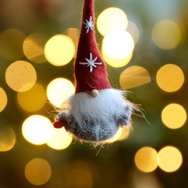 Till vänster ett dignande julbord med julskinka senap bröd fikon och tända ljus bredvid en julgran och till höger en filtad jultomte som hänger i en gran med julgransbelysning bakom