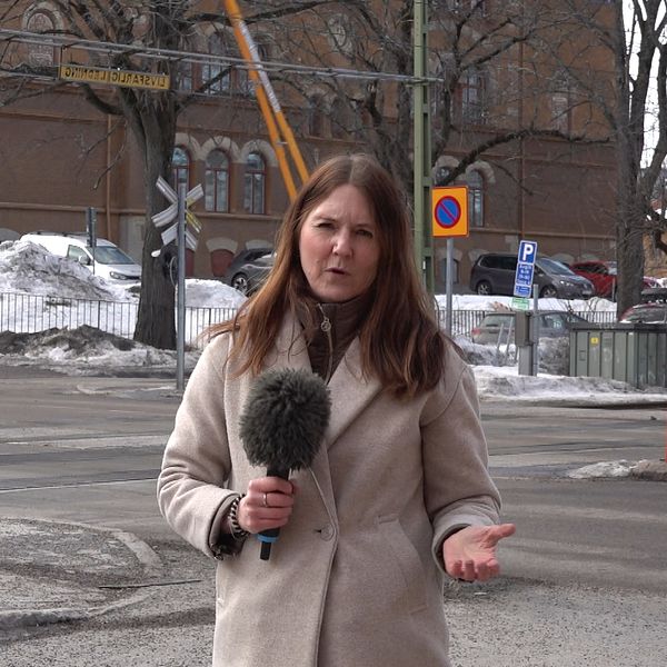 SVT Västernorrlands reporter Anna Beijron står vid plankorsningen på Skolhusallén i Sundsvall bakom henne fälls järnvägsbommarna