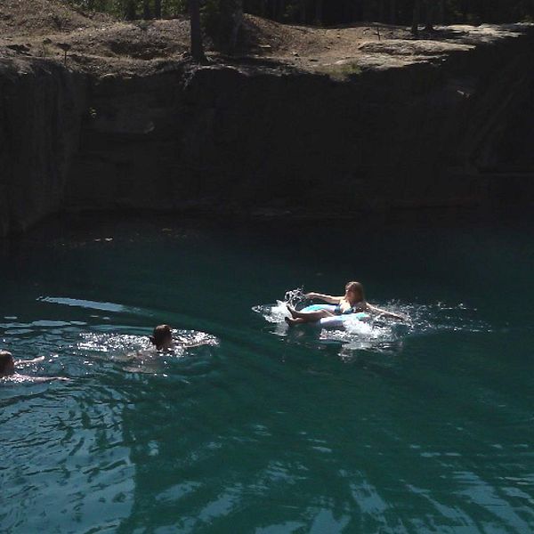 tre personer som simmar i grönt vatten framför en klippkant