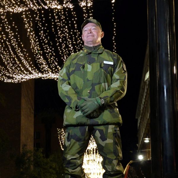 Lars Bergman i camouflagedräkt står uppställd på en gatan där julbelysning hänger ovanför. Omgivningen är mörk med ljusa dekorationer som skapar en festlig stämning.