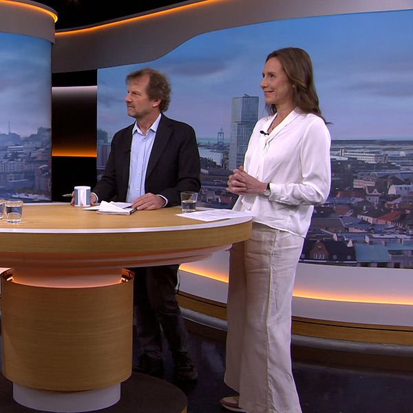 Tre personer står vid ett runt bord i en tv-studio under ett samtal.