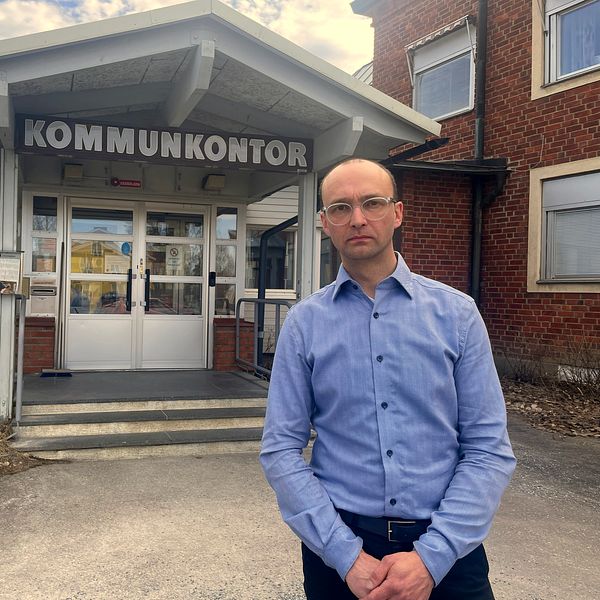 Bjurholms kommunchef Jimmy Johansson står i blå skjorta framför kommunkontoret med bister uppsyn.