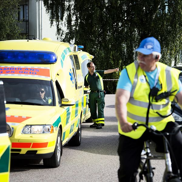 Två ambulanser står parkerade på en asfalterad väg. En man med reflexväst cyklar i förgrunden.