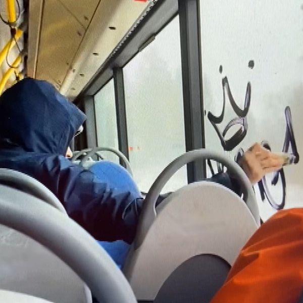 Till vänster står kommunpolisen Henrik Blusi och till höger ser man personen som klottrar på ett fönster i en linjebuss i Sundsvall.