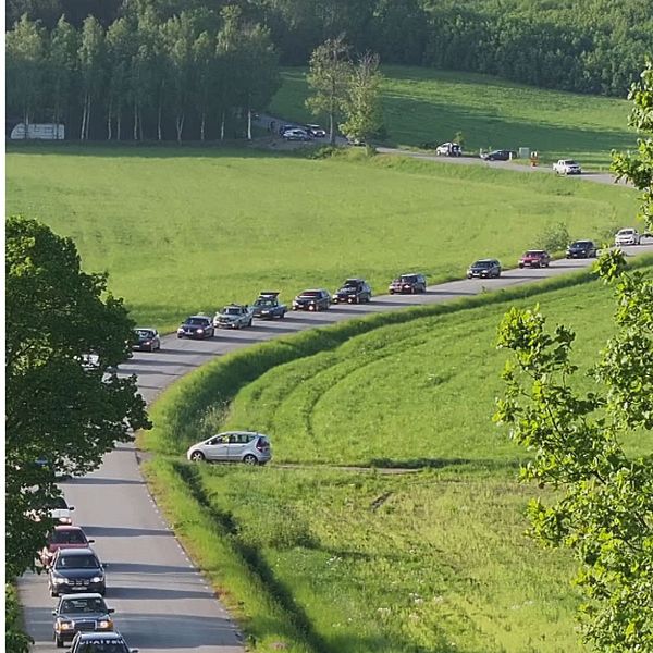 En lång kortege av A-traktorer och personbilar åker längs slingriga vägar omgivna av grönska.