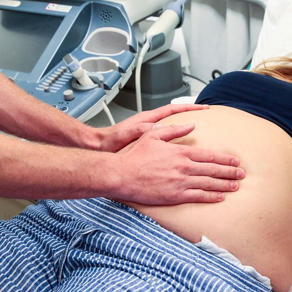 Läkaren Joline Asp intervjuas med mikrofon. En gravid kvinna undersöks på magen.