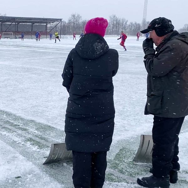 Personer ser på en fotbollsmatch under vintriga förhållanden på en snötäckt plan.