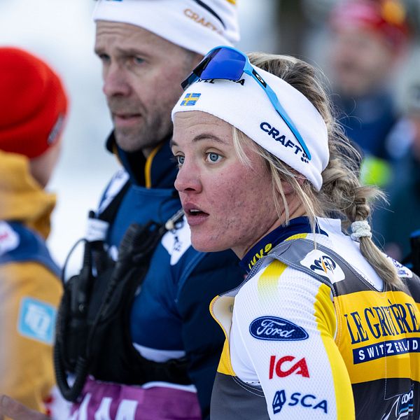 En delad bild visar en skidåkare i rörelse på vänster sidan, iförd en blå och gul tävlingsdräkt. På höger sidan står flera personer i diskussion, iklädda skidkläder och hjälmar, vilket indikeras av deras klädval och utrustning.