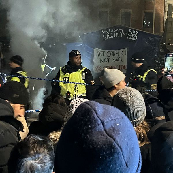 En tvådelad bild. Bilden till vänster visar en reporter med en mikrofon i handen med texten SVT på. Reportern har glasögon, en blå mössa och en grå jacka. Bilden till höger visar en scen som utspelar sig framför en byggnad tillhörande Göteborgs universitet. En rad dialogpoliser står på ena sidan om ett avspärrningsband. På andra sidan står en större mängd demonstranter. Rök stiger från marken bakom poliserna.
