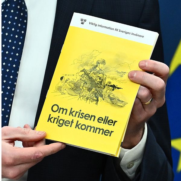 till vänster syns hesa fredrik och till höger håller en man i msb:s nya broschyr ”om krisen eller kriget kommer”