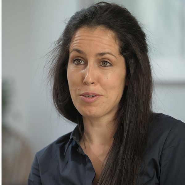 Schimpans hoppar ner från en gren. Kvinna i mörkblå skjorta.