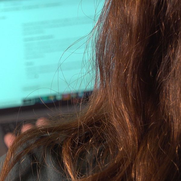 En person med långt hår sitter vid ett skrivbord och använder en laptop, hon är inne på sidan chatgpt. På bordet ligger ett block och en penna. Skärmen visar text, vilket tyder på arbete eller studier.