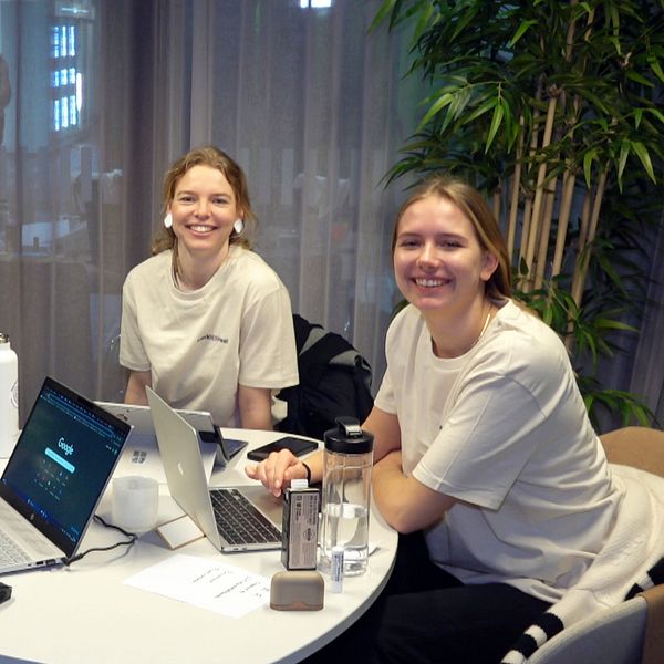 Tre kvinnor vid ett runt bord med datorer framför sig ler in i kameran