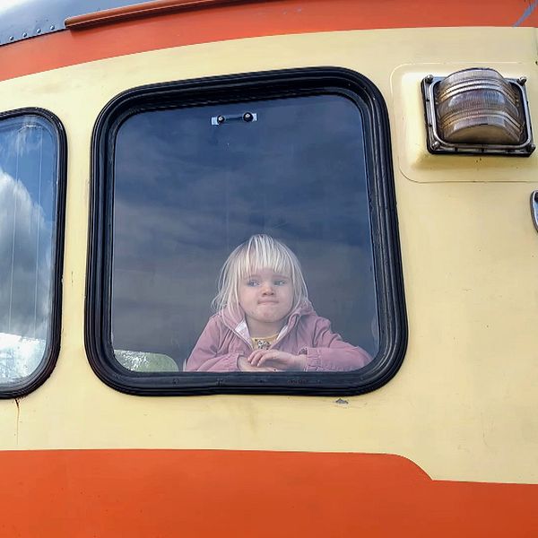 Litet barn tittar ut genom fönstret på ett orangegult tåg.
