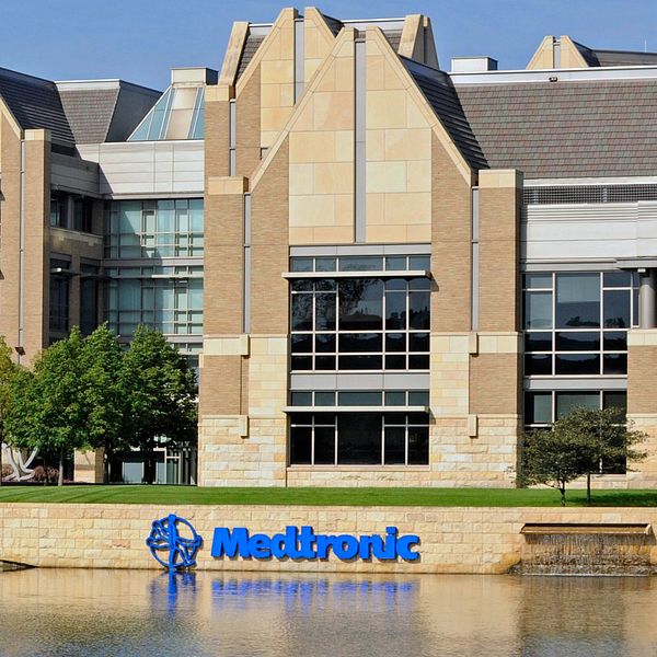 Urgent Field Safety Notices från Medtronic som gäller det robotassisterade kirurgiska systemet, placerade bredvid Medtronics kontorsbyggnad med en insjö i förgrunden.