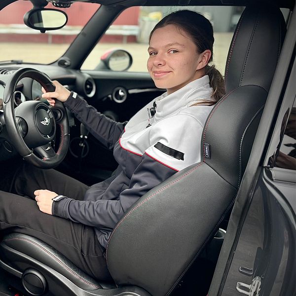 Person sitter i förarsätet på en bil iklädd en svart och grå uniform.
