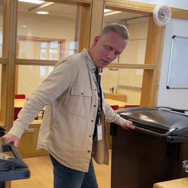 En man håller i två soptunnor i en korridor