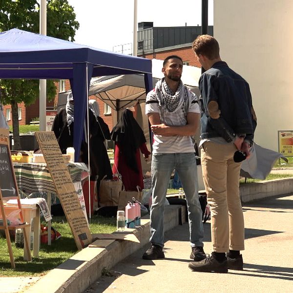 En man står och pratar med en manlig reporter på ett campusområde.
