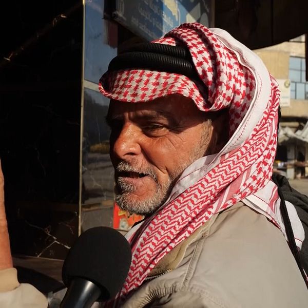 En man klädd i rödvit keffiyeh-sjal pratar in i en mikrofon