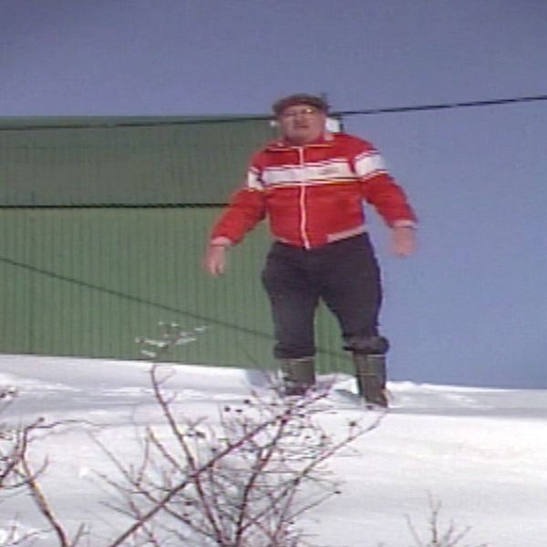 En man står på en stor snödriva bredvid sitt hus.