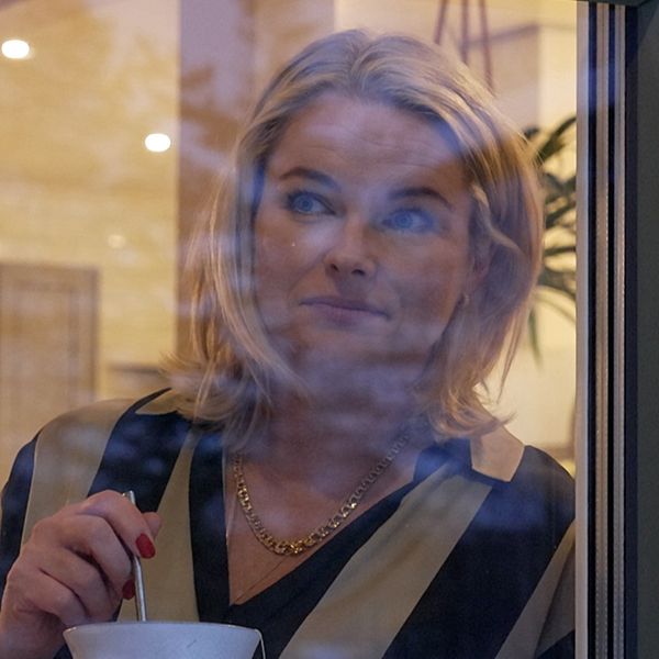 En kvinna tittar ut genom ett fönster och håller i sin tekopp.